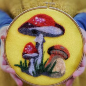 ricamo di funghi stile pop art con lana cardata su pannolenci giallo e incorniciato con un telaio da ricamo tondo